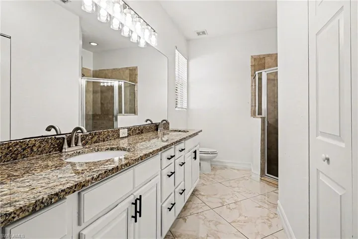 Full bathroom with double vanity, a stall shower, and light marble finish flooring