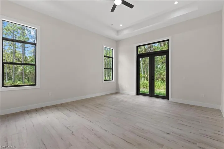 Tray ceiling, wood-finish flooring, recessed lighting, ceiling fan, and black-framed glass French doors