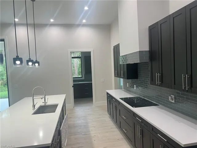Kitchen featuring a large island with an integrated sink, dark cabinetry, light countertops, and a gray subway tile backsplash