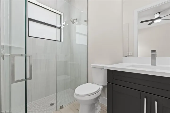 Glass-enclosed shower with a rainfall showerhead, modern vanity with a white countertop, chrome faucet, and wood-finish flooring