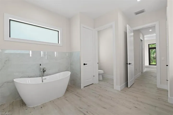 Freestanding soaking tub with floor-mounted faucet, large format tile wall, and wood-finish flooring