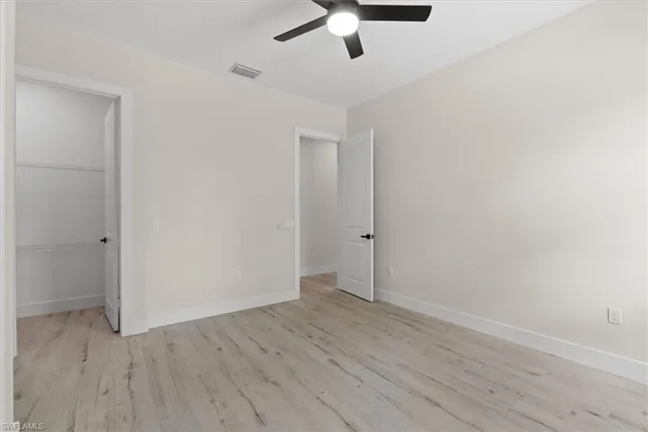 Spacious room featuring wood-finish flooring, light-toned walls, a ceiling fan, and a built-in closet with shelving