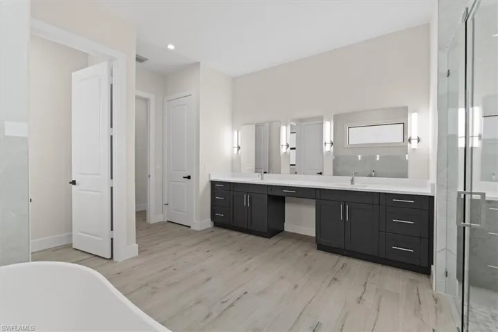 Dual vanities with undermount sinks, wood-finish flooring, glass-enclosed shower, and a freestanding bathtub