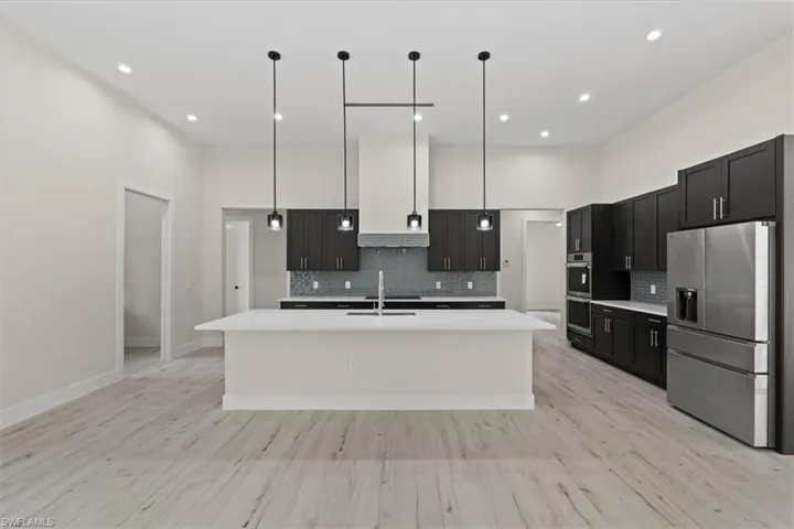 Open-concept kitchen with a large island, wood-finish flooring, dark cabinetry, and stainless steel appliances