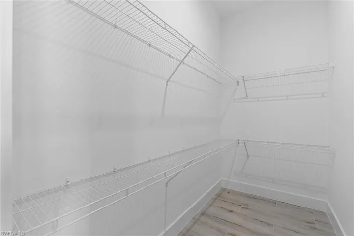 White wire shelving system, light gray wood-finish flooring, white walls, and bright overhead lighting