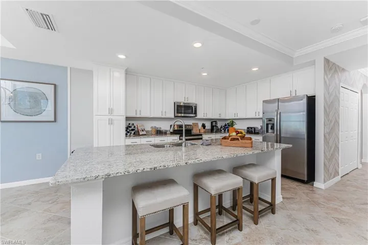 Kitchen featuring visible vents, a sink, stainless steel appliances, white cabinetry, and a kitchen bar