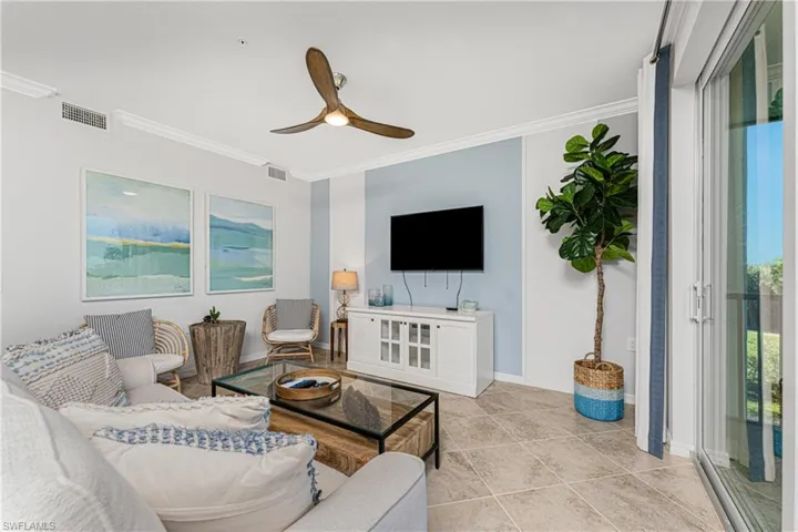Living room with crown molding, baseboards, visible vents, and ceiling fan