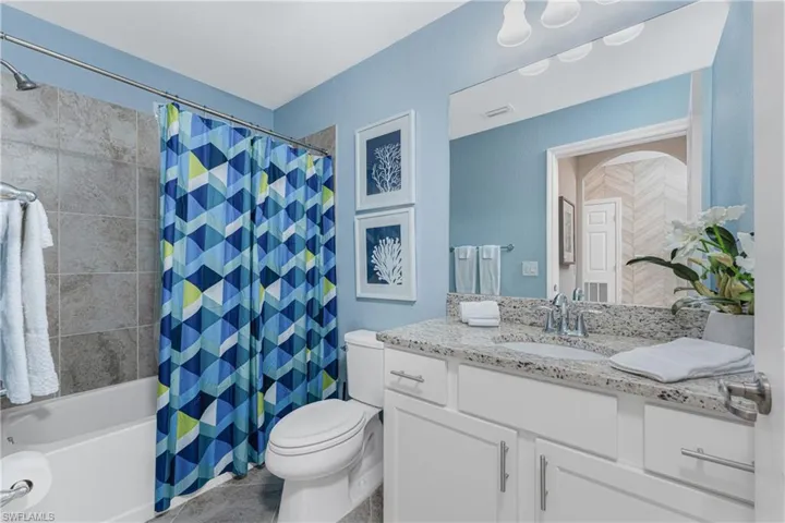 Bathroom featuring tile patterned flooring, shower / bath combination with curtain, toilet, and vanity