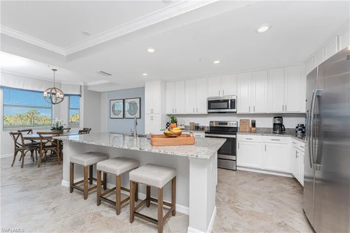 Kitchen featuring an island with sink, light stone counters, appliances with stainless steel finishes, white cabinets, and crown molding