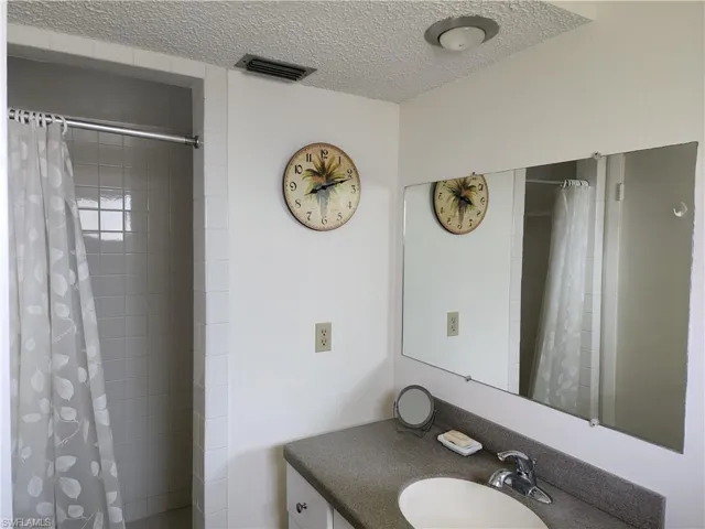 Full bathroom featuring vanity, a textured ceiling, and tiled shower