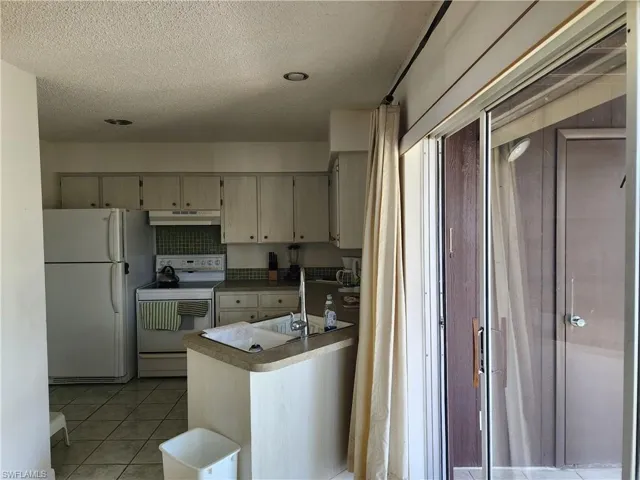 Kitchen featuring white appliances, light tile patterned floors, a textured ceiling, under cabinet range hood, and light countertops