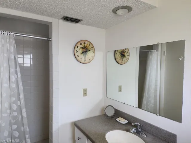 Full bath with vanity, tiled shower, and a textured ceiling