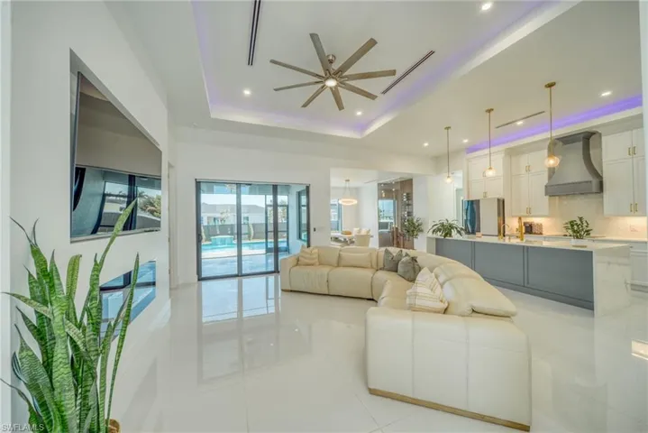Living area featuring ceiling fan, light tile patterned floors, a raised ceiling, and recessed lighting