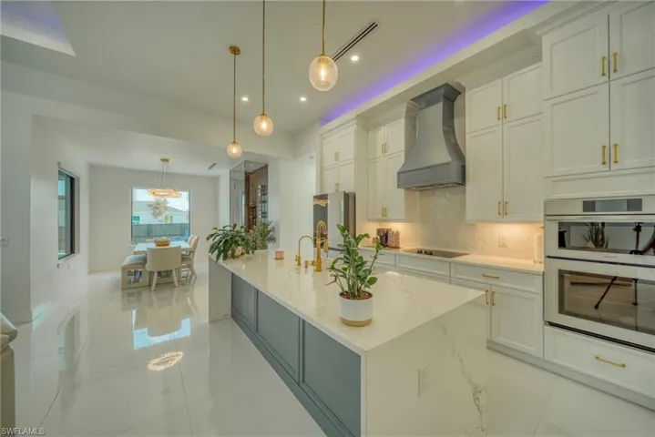 Kitchen with white cabinetry, tasteful backsplash, light stone counters, and a large island
