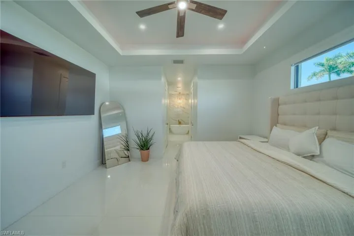Bedroom featuring a raised ceiling, ceiling fan, light tile patterned flooring, recessed lighting, and connected bathroom
