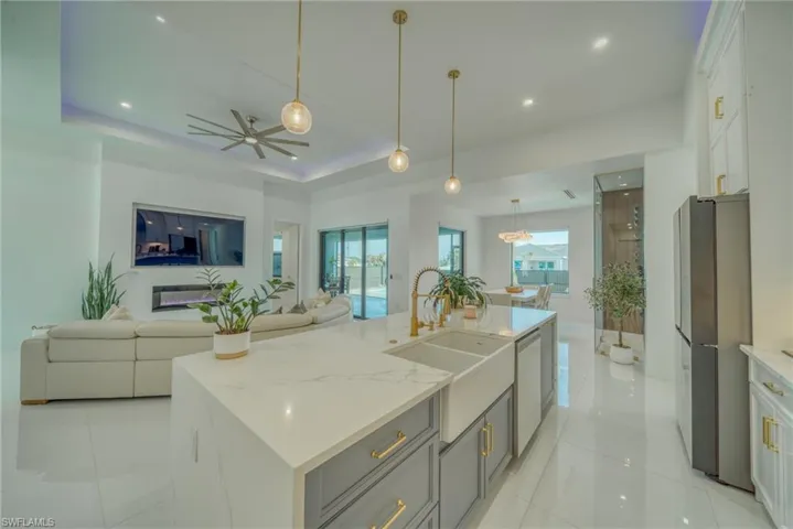 Kitchen with open floor plan, an island with sink, light stone countertops, freestanding refrigerator, and a tray ceiling