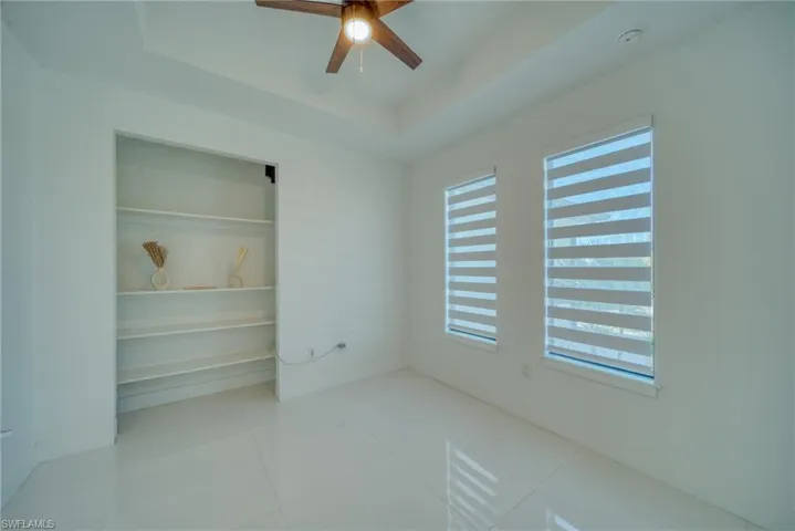 Unfurnished bedroom with a closet, a tray ceiling, a ceiling fan, and light tile patterned floors