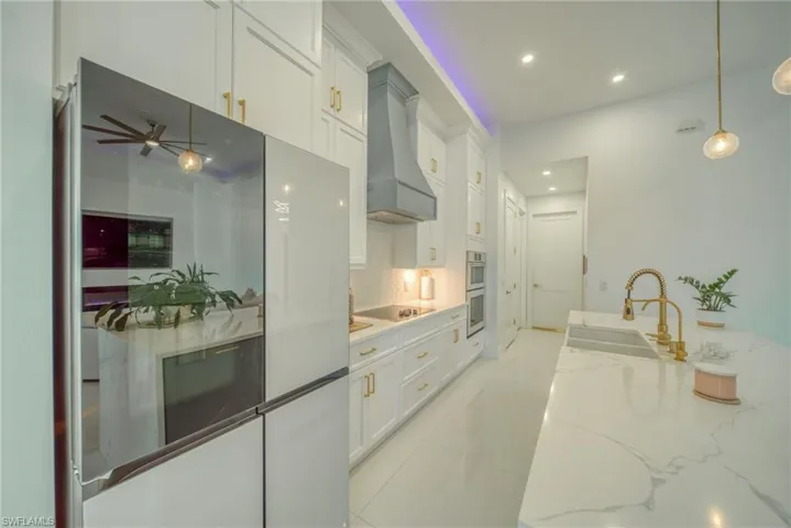 Kitchen with white cabinetry, freestanding refrigerator, hanging light fixtures, light stone countertops, and backsplash