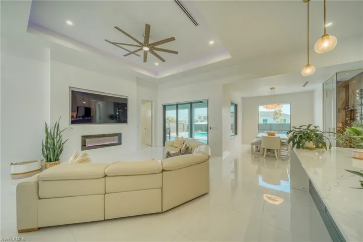 Living room with a ceiling fan, light tile patterned flooring, a raised ceiling, recessed lighting, and a glass covered fireplace