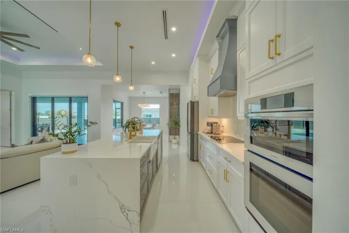 Kitchen with open floor plan, white cabinets, stainless steel appliances, light stone counters, and a large island
