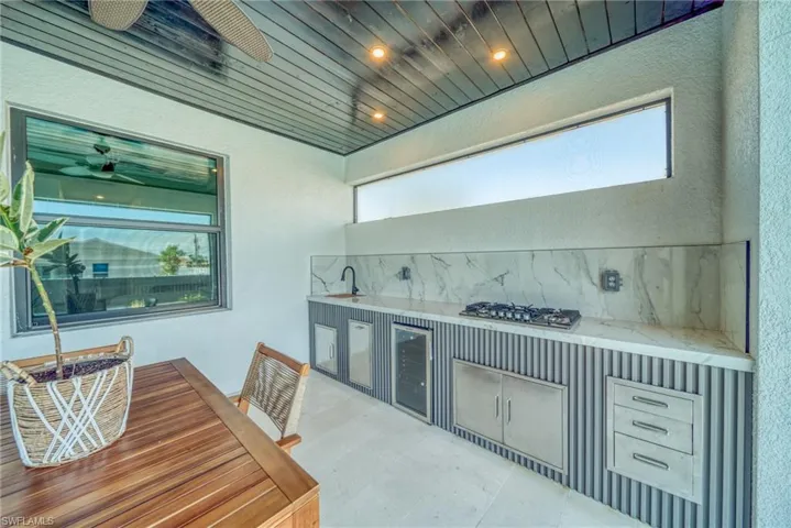 Indoor wet bar featuring tasteful backsplash, stainless steel gas cooktop, wine cooler, recessed lighting, and a textured wall