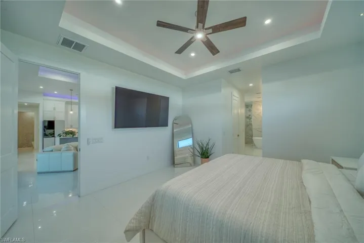 Bedroom with a tray ceiling, recessed lighting, a ceiling fan, light tile patterned flooring, and arched walkways