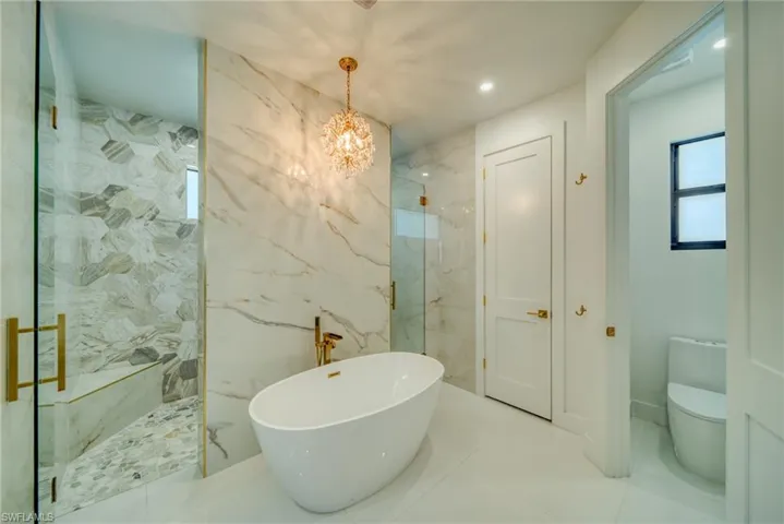 Bathroom featuring a marble finish shower, a freestanding tub, hanging lights, light tile patterned floors, and tile walls