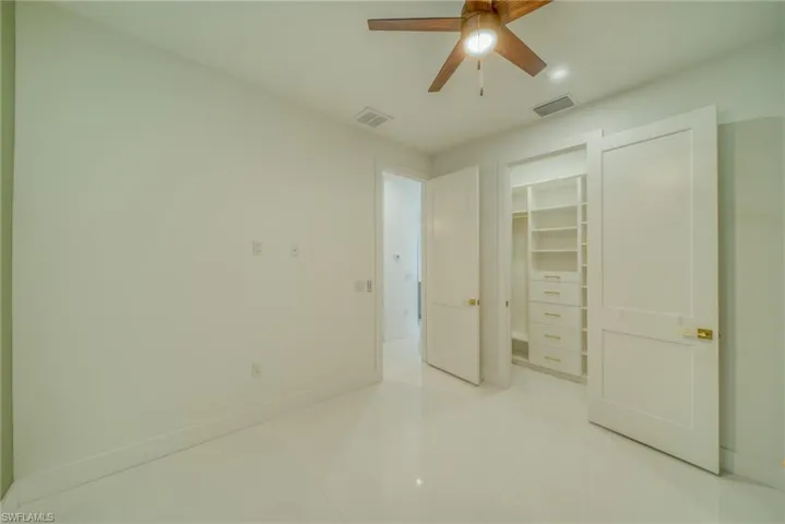 Unfurnished bedroom featuring a spacious closet, light tile patterned floors, and a ceiling fan