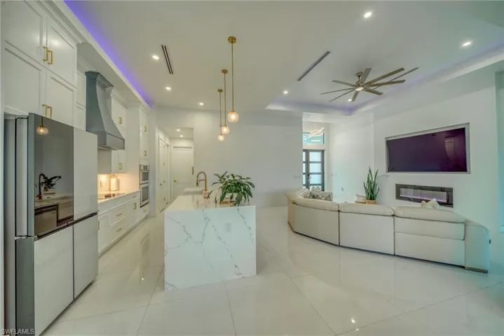 Kitchen featuring stainless steel appliances, white cabinets, light tile patterned floors, open floor plan, and light stone countertops