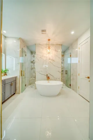 Full bathroom featuring a soaking tub, a marble finish shower, vanity, hanging lights, and tile walls