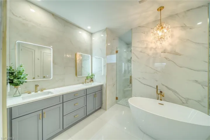 Bathroom featuring a freestanding bath, stone wall, double vanity, a marble finish shower, and tile walls