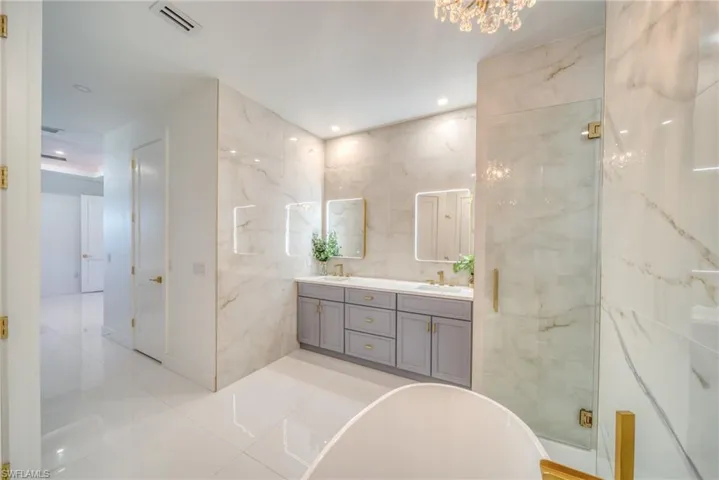 Full bathroom featuring double vanity, a freestanding bath, a marble finish shower, tile walls, and hanging lights