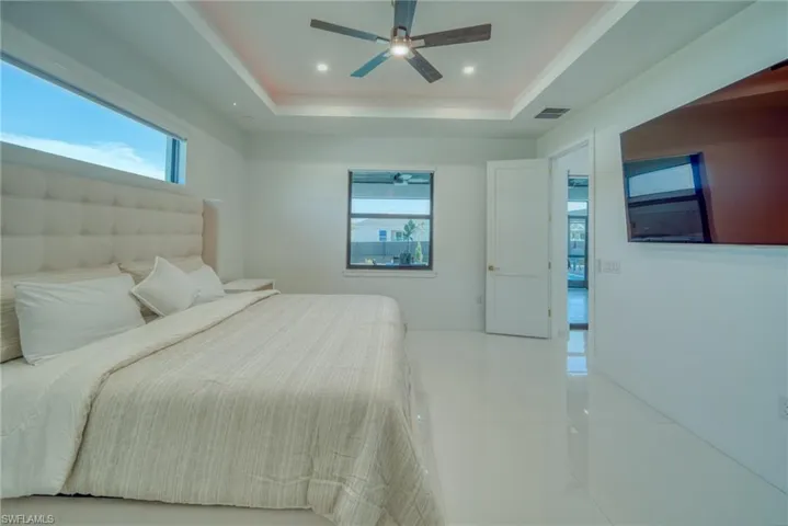 Bedroom featuring multiple windows, light tile patterned floors, a ceiling fan, recessed lighting, and a tray ceiling