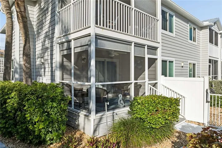 Two-story exterior featuring light-colored horizontal siding, a screened-in ground-level porch, a second-story balcony with white railings, and vinyl privacy fencing