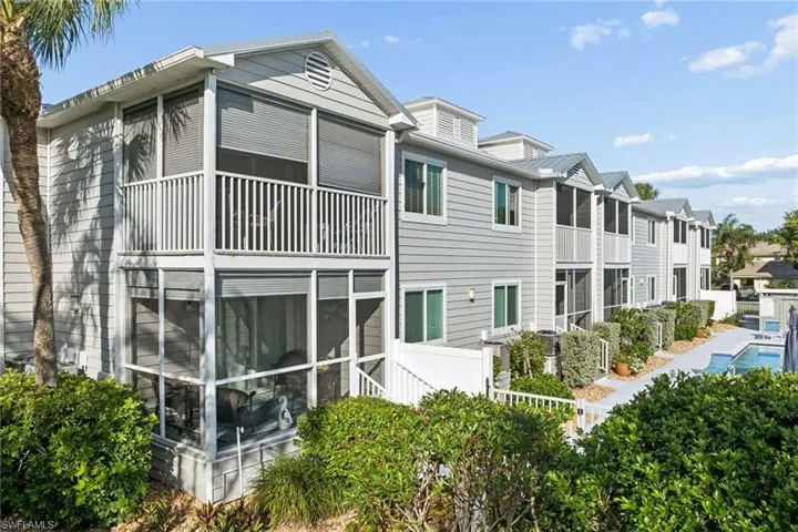 Multi-story exterior with light gray siding, dual-level screened lanais, white vertical railings, and a metal roof