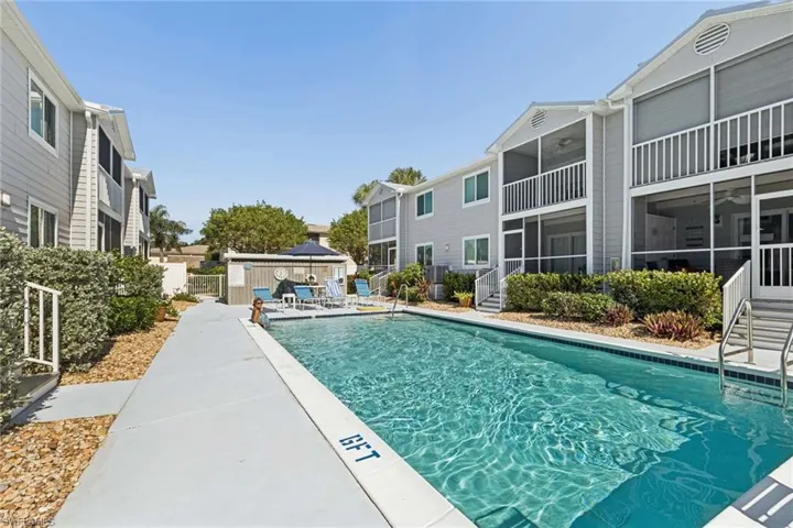 In-ground swimming pool with concrete decking, multi-story buildings featuring lap siding, and screened-in balconies