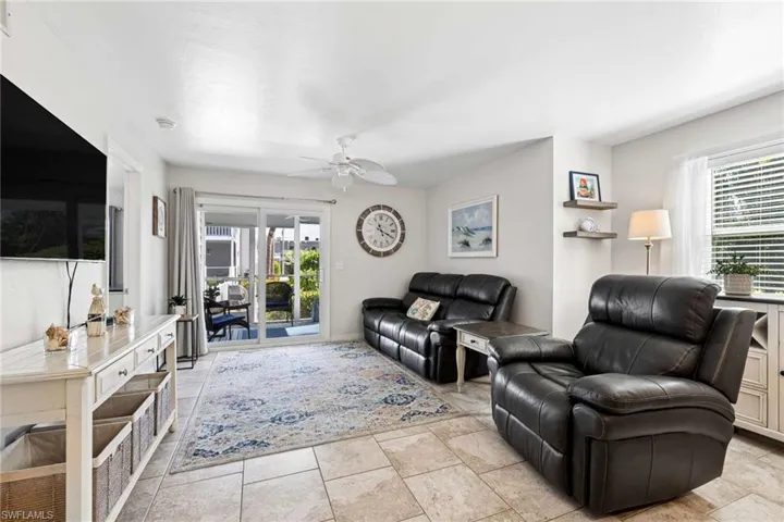 Living area featuring large-format neutral tile flooring, sliding glass patio doors, a ceiling-mounted fan, and built-in wall shelving