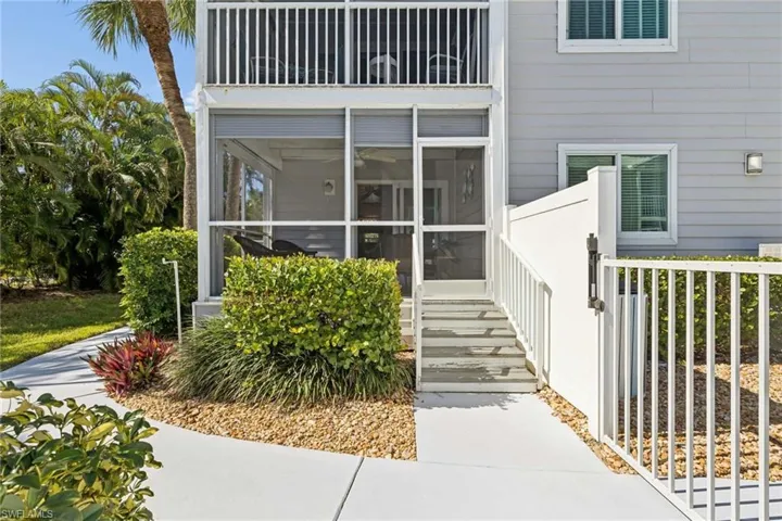 Multi-level exterior featuring a screened-in lanai, concrete walkway, private outdoor staircase, and white vinyl privacy fencing