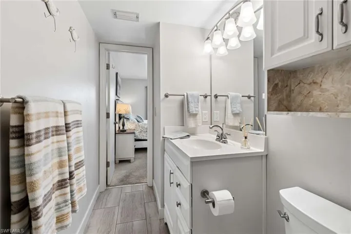 Bathroom vanity with white cabinetry, integrated sink, polished chrome faucet, multi-light fixture, and stone-finish backsplash