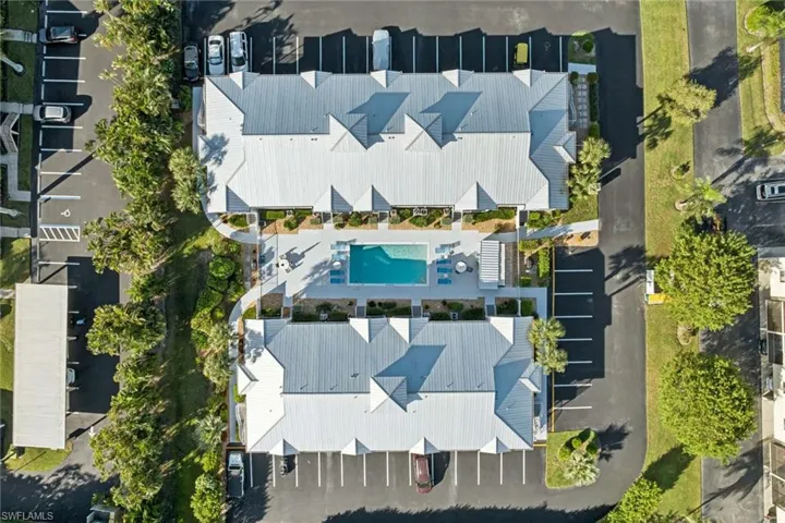Aerial perspective featuring metal-roofed buildings, a central outdoor swimming pool, dedicated paved parking areas, and mature landscaping