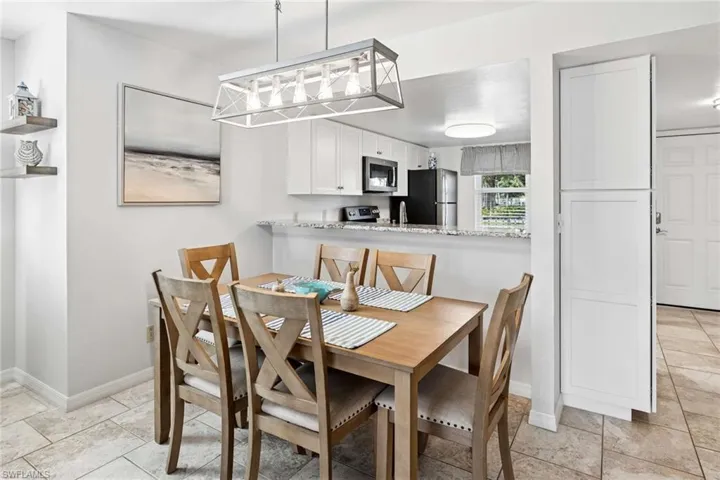 Dining area featuring tile flooring, a rectangular light fixture with a metallic frame, and a pass-through opening to the kitchen with stone-finish countertops and white cabinetry
