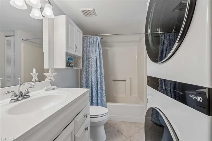 Bathroom featuring a white vanity cabinet, solid-surface countertop with an integrated basin, wall-mounted storage cabinetry, tiled flooring, and a combined tub and shower surround