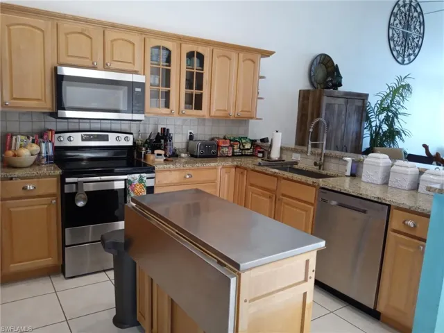 Kitchen featuring stainless steel appliances, glass insert cabinets, light brown cabinets, and a peninsula