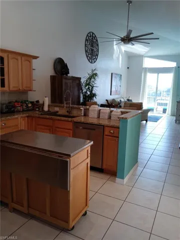 Kitchen with open floor plan, a peninsula, dishwasher, light tile patterned flooring, and high vaulted ceiling