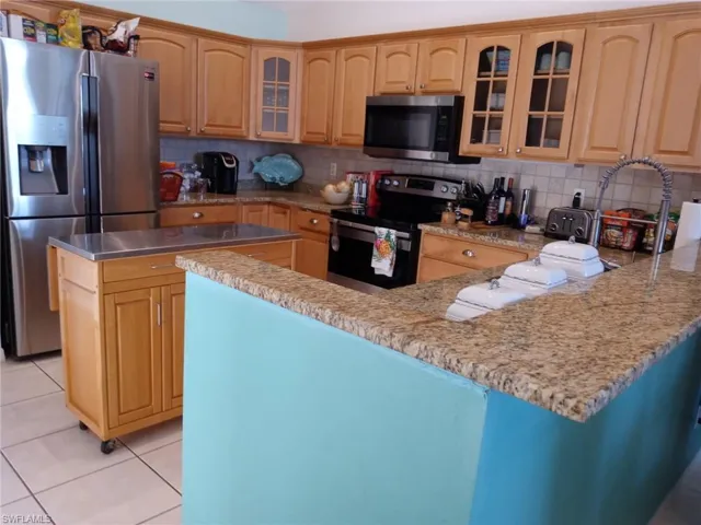 Kitchen with glass insert cabinets, appliances with stainless steel finishes, a peninsula, decorative backsplash, and light stone countertops