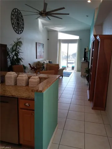 Kitchen featuring light stone counters, stainless steel dishwasher, brown cabinets, lofted ceiling, and ceiling fan