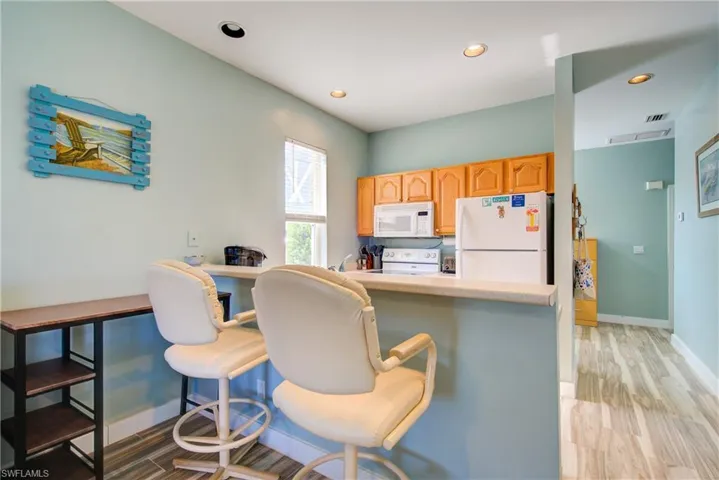 Kitchen with white appliances, light countertops, light brown cabinets, recessed lighting, and a breakfast bar area