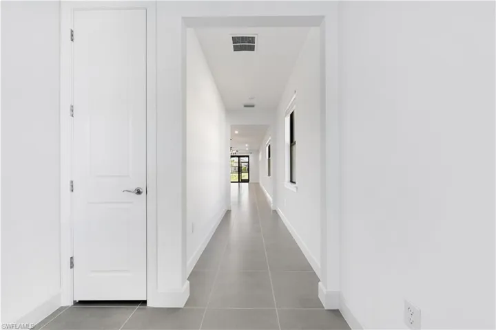 Entryway hallway featuring light gray tile flooring, recessed lighting, white walls, white baseboards, and a white interior door with a chrome lever handle
