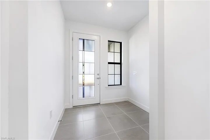 Foyer featuring a paneled glass entry door, a grid-paned side window with black trim, recessed ceiling lighting, and square tile flooring