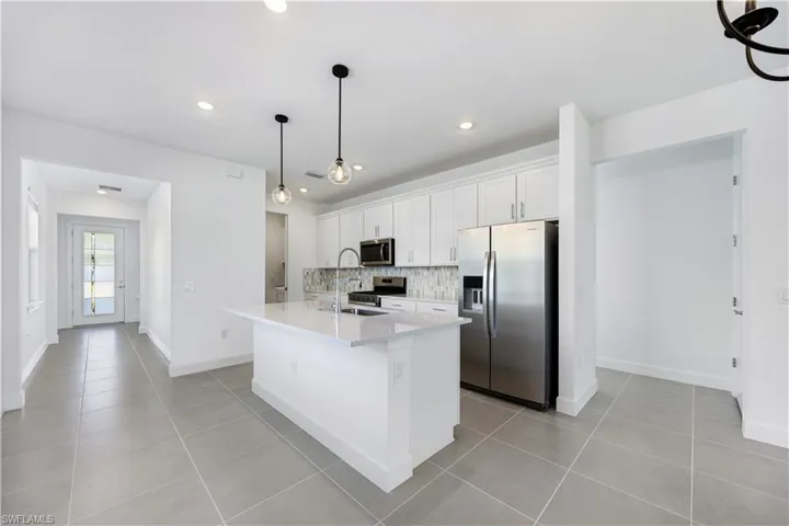 Kitchen featuring a central island with a sink, stainless steel appliances, white cabinetry, a mosaic tile backsplash, and recessed lighting
